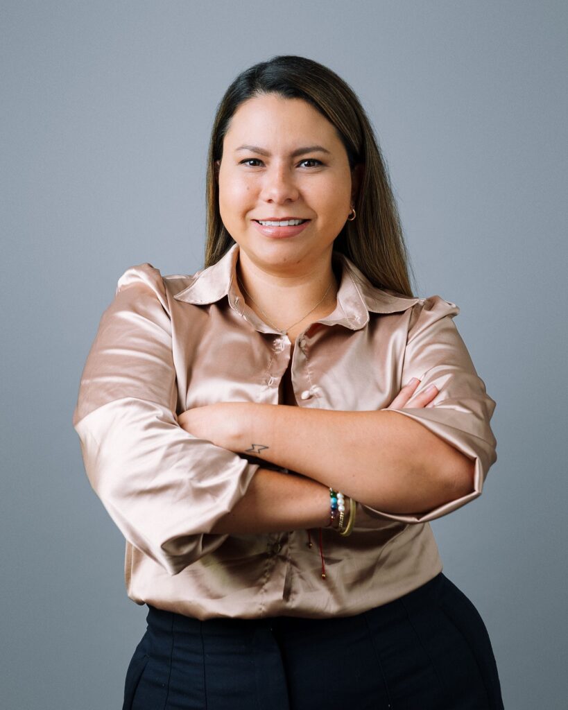 Retrato profesional de una mujer con blusa satinada rosa, brazos cruzados